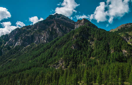A beautiful scenery of high rocky mountains covered with green trees under the cloudy sky at Pragelato, Italyの写真素材
