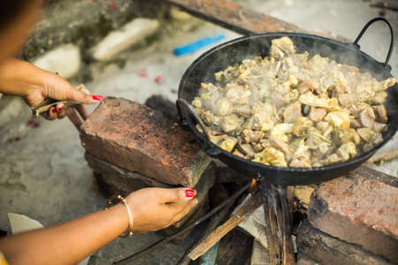 A female making a meal with meat and vegetables in a black pan on wood fire stove