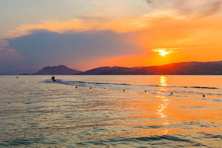 A beautiful shot of a person riding a motorboat in the sea with the reflection of the sunset in Skiathos Greeceの写真素材