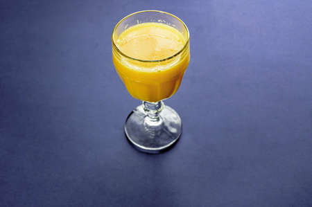 A high angle shot of an orange juice in a glass on a dark blue surface
