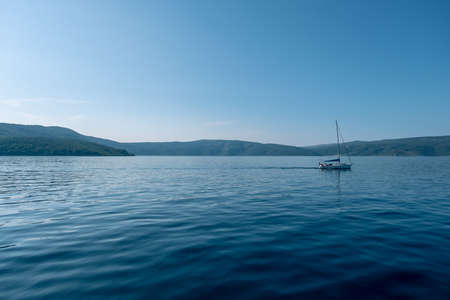 A single ship on the middle of the sea surrounded by high rocky mountainsの写真素材