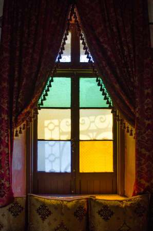 A vertical shot of a window sill with beautiful red and gold curtains and colorful glassの写真素材