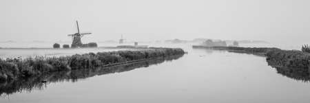 Black and white landscape photo of a typical Dutch scenery. There are some historic windmills in the photo.の写真素材
