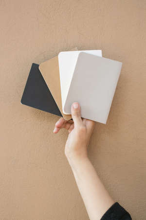 A vertical shot of a person holding four notepads on a brown background