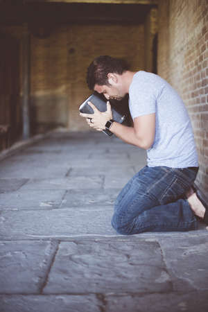 A vertical shot of a male on his knees on the ground with the bible against his head praying