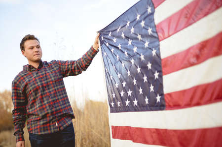 A white male holding the flag of the United States of America during sunrise