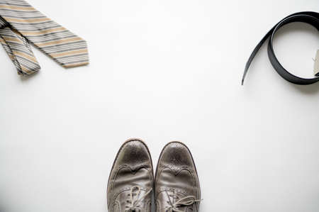 An overhead shot of a white surface with shoes, belt and a tie over itの写真素材