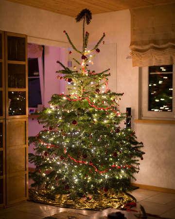 A beautifully decorated Christmas tree with ornaments and string lights inside a room - Christmas is coming conceptの写真素材