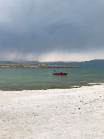 A vertical shot of a lonely person paddling in a red boat in the sea under the foggy sky