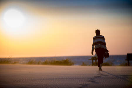 A beautiful shot of a female walking on a sandy shore leaving footprints behindの写真素材