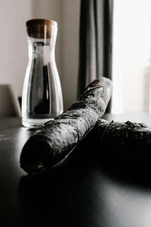 A vertical shot of two black breads near a bottle on a table