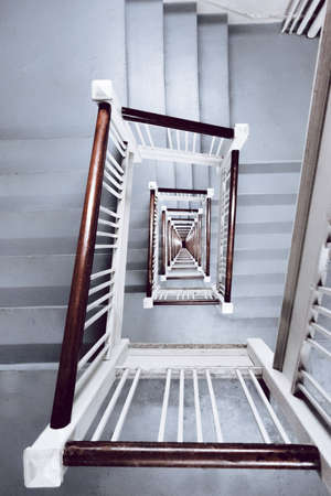 A vertical high angle shot of a white stairway with wooden handrails