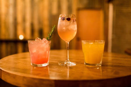 A wooden table with three glasses of different cocktails on a blurred background