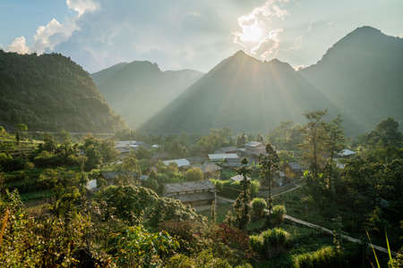 A high angle shot of a cabin near green trees surrounded by high mountains under the bright sun in Vietnamの写真素材