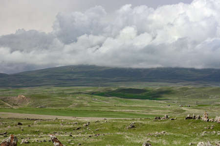 A beautiful shot of a landscape surrounded by high mountains under the storm clouds