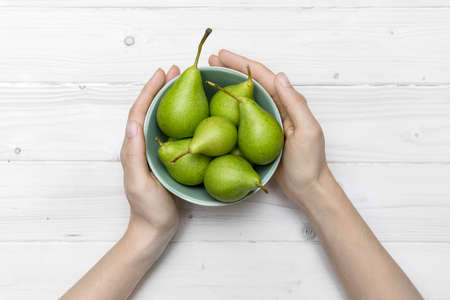 A high angle shot of a person holding a green bowl of pears on a white wooden surfaceの写真素材