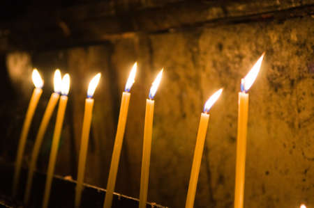 A selective focus shot of burning yellow candles inside the churchの写真素材