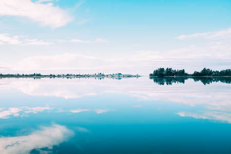 A beautiful scenery of a range of trees reflecting in the lake under the cloudy skyの写真素材