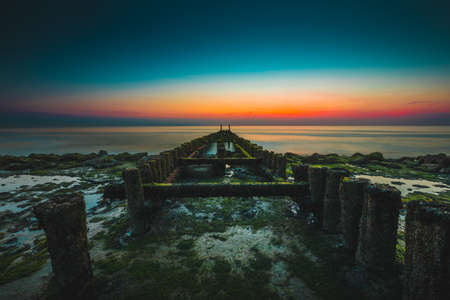 A moss covered wooden pier under the beautiful sky captured in Westkapelle, Netherlandsの写真素材