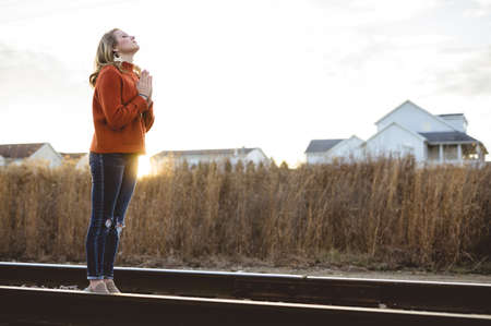 A female praying while standing on the train rails