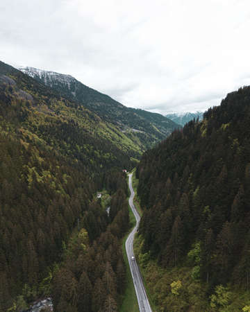 A vertical aerial shot of a road going through the tree covered mountains under a cloudy skyの写真素材