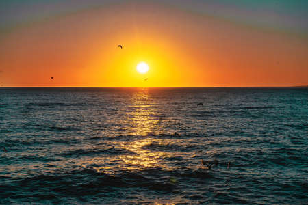 A beautiful sunset reflecting on a sea with seagulls flying above the wavesの写真素材