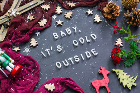 A high angle shot of a dark surface with an inscription baby it's cold outside surrounded by festive...