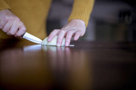 A closeup shot of a female slicing up onion on a wooden surface with a blurred backgroundの写真素材