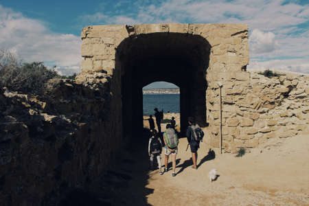 A beautiful shot of people walking through a small brick tunnel near the sea with a cloudy sky in the backgroundのeditorial素材