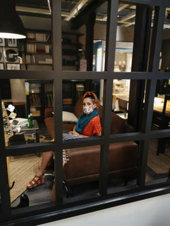 A vertical shot of a young female wearing a medical mask sitting at home