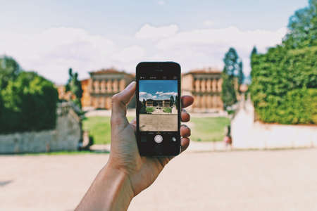 A person with a smartphone taking a picture of the beautiful view with high buildings surrounded by green treesのeditorial素材