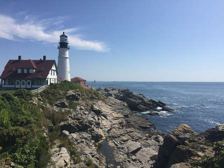 A beautiful shot of a lighthouse near the building and the sea with a blue sky in the background