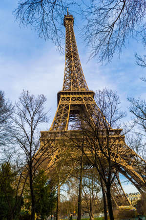 A low angle shot of Eiffel tower surrounded by trees with the background of the cloudy skyのeditorial素材