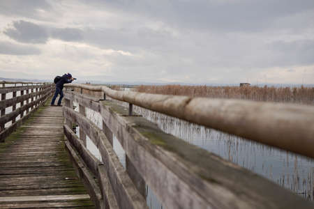 MAGIONE, ITALY - Jan 05, 2016: Man on a wooden bridge photographing the landscape of the naturalistic oasis of  "La valle" in the lake of Trasimeno in a cloudy day,  Magione, Umbriaのeditorial素材
