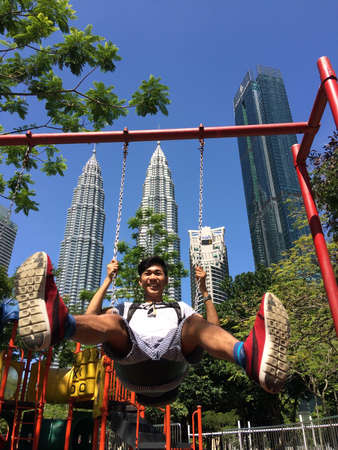 A vertical low angle shot of a male swinging on the background of skyscrapersのeditorial素材