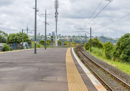 AUCKLAND, NEW ZEALAND - Dec 12, 2015: A wide shot of a train track near an asphalt road surrounded by green trees in Auckland, New Zealandのeditorial素材