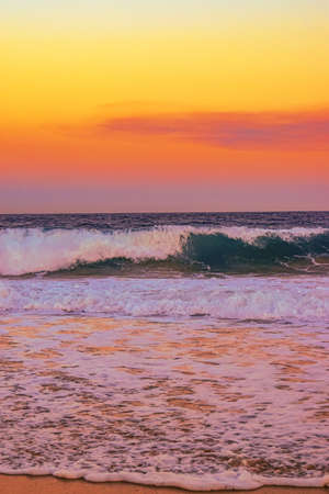 A landscape of a beach surrounded by sea waves during an orange sunset in the evening