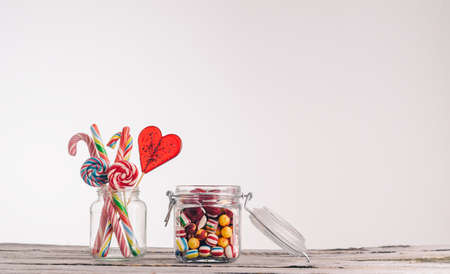 A closeup shot of candy canes and other candies in glass jars on a wooden surface - perfect for a...