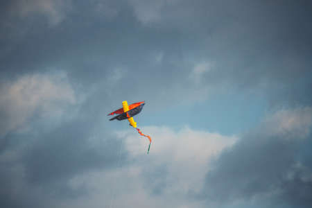 A colorful kite flying in the blue cloudy sky - a cool picture for backgrounds and wallpapersの写真素材