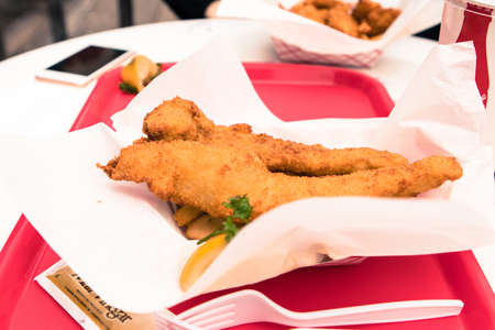 A selective focus shot of chicken fillets and fries on a red platterの写真素材