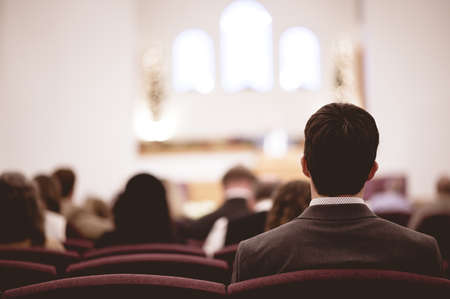 A male wearing a suit and other people sitting in a church