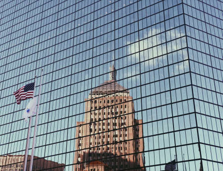 A beautiful wide shot of glass skyscraper building with the American flag and a tall building reflection on it in Bostonの写真素材