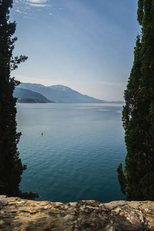 The sea surrounded by greenery with hills under sunlight and a blue sky on the background