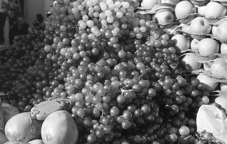A grey scale shot of delicious grapes and apples in a fruit market