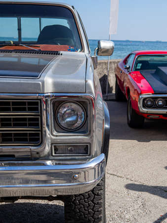 A vertical shot of the headlights and the hoods of two silver and red automobiles