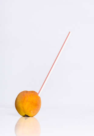 A vertical shot of a juice straw in a peach reflecting on a white backgroundの写真素材