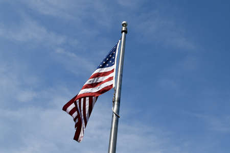 A low angle view of the American flag near trees under a blue cloudy sky and sunlightの写真素材