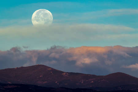 A beautiful scenery of a mountain range with the moon and white clouds in the backgroundの写真素材