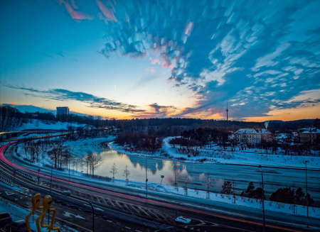 A landscape of roads surrounded by greenery and buildings covered in the snow during sunsetの写真素材