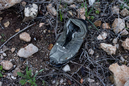 A high angle shot of an old and torn out shoe left behind on a path covered with rocks and pebblesの写真素材